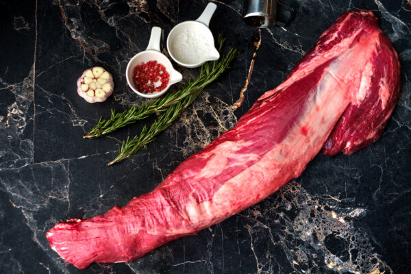 fresh raw beef tenderloin on a marble table with seasonings and rosemary, a whole uncut piece