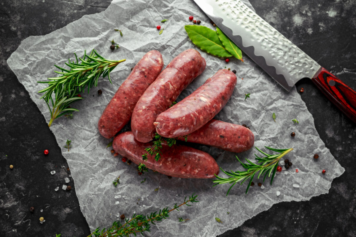 Freshly made raw breed butchers sausages in skins with herbs on crumpled paper